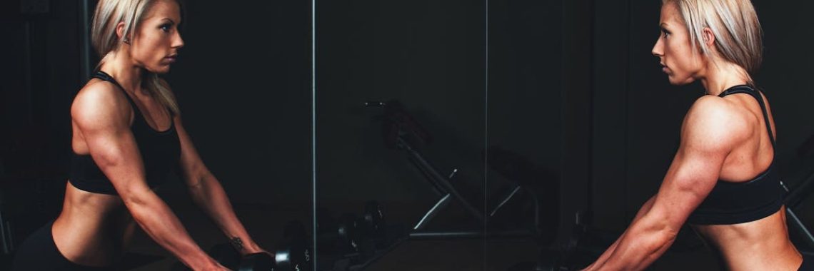 Athletic woman engaging in strength training exercise with dumbbells in a gym setting, reflecting on progress.